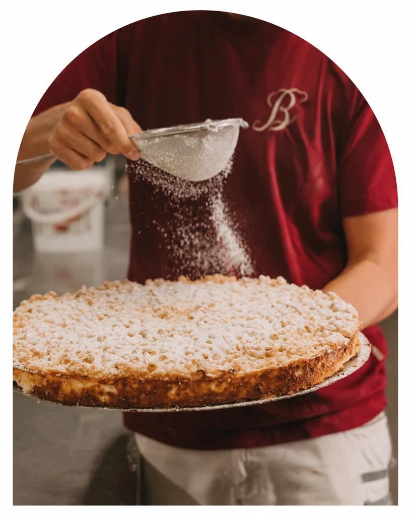 Puderzucker wird über einen runden Streusselkuchen verteilt.