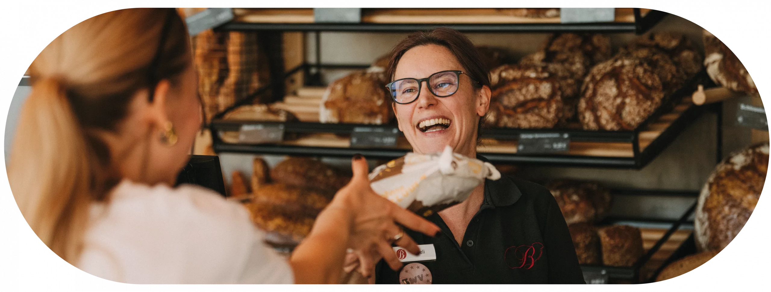 Verkäuferin in einer Bäckerei Burkard Filiale am übergeben einer Bestellung. Sie lacht in die Kamera.