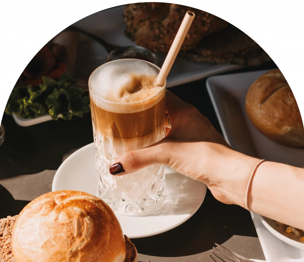 Eine Hand greift nach einem Latte Macchiato.
