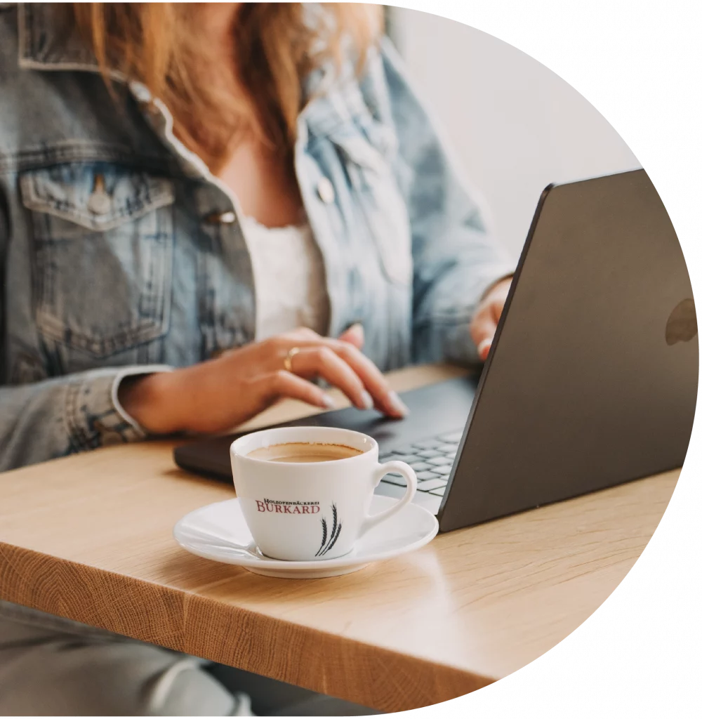 Ein Workspace bei der Bäckerei Burkard. Eine Frau trinkt einen Kaffee und schriebt etwas mit ihrem Laptop.